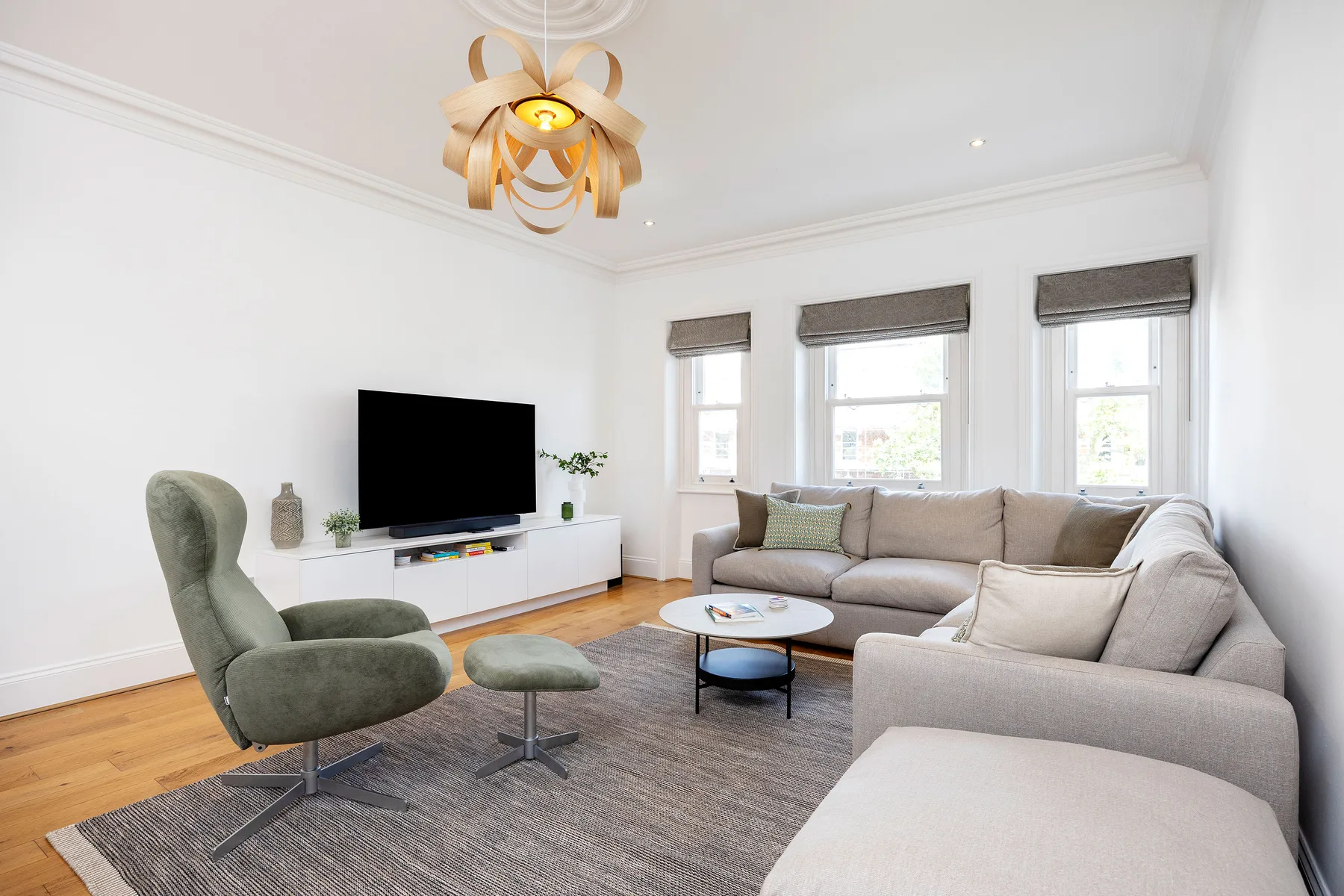 Una sala luminosa con sofá seccional, televisor y ventanas.