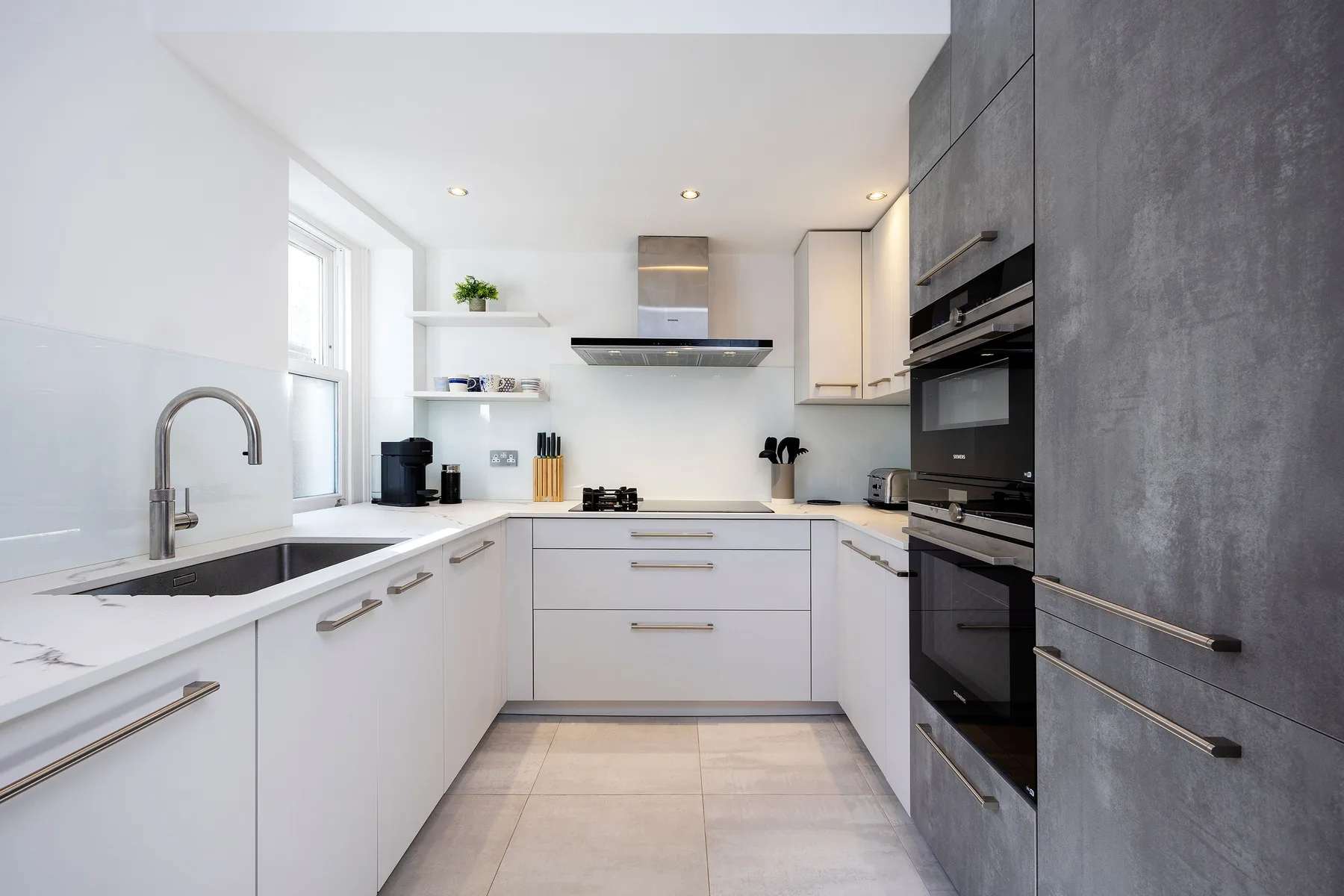 Una cocina moderna con gabinetes blancos, electrodomésticos oscuros y una zona de cocción central.