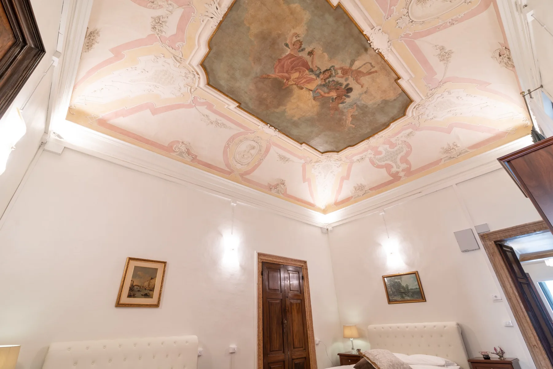Una sala de estar con molduras rosas ornamentadas y un panel pintado en el techo.