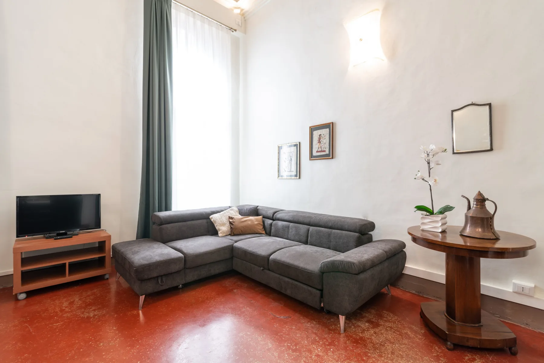 Una sala de estar con un sofá seccional gris, televisor y mesa redonda de madera.