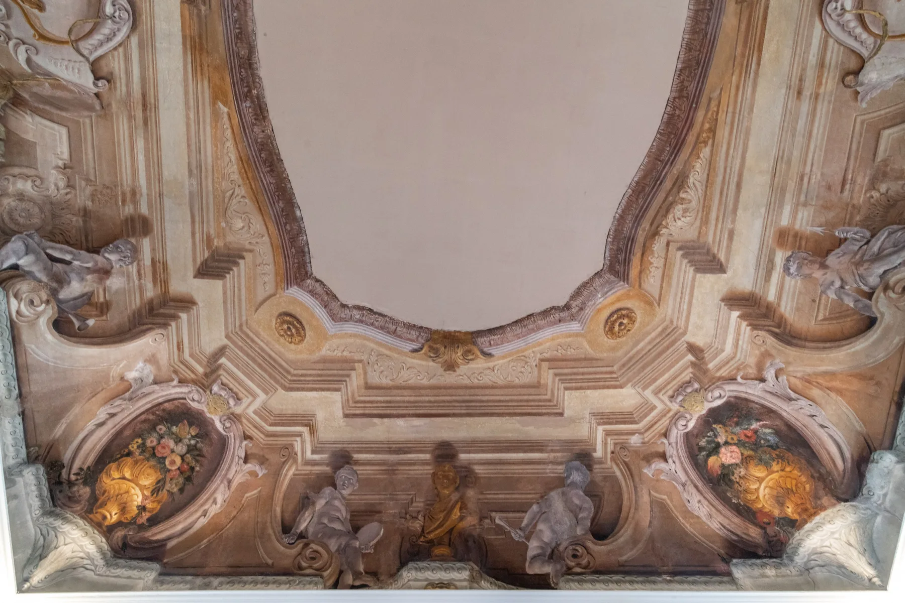 Un techo ornamentado con figuras esculpidas, molduras decorativas y paneles florales pintados.