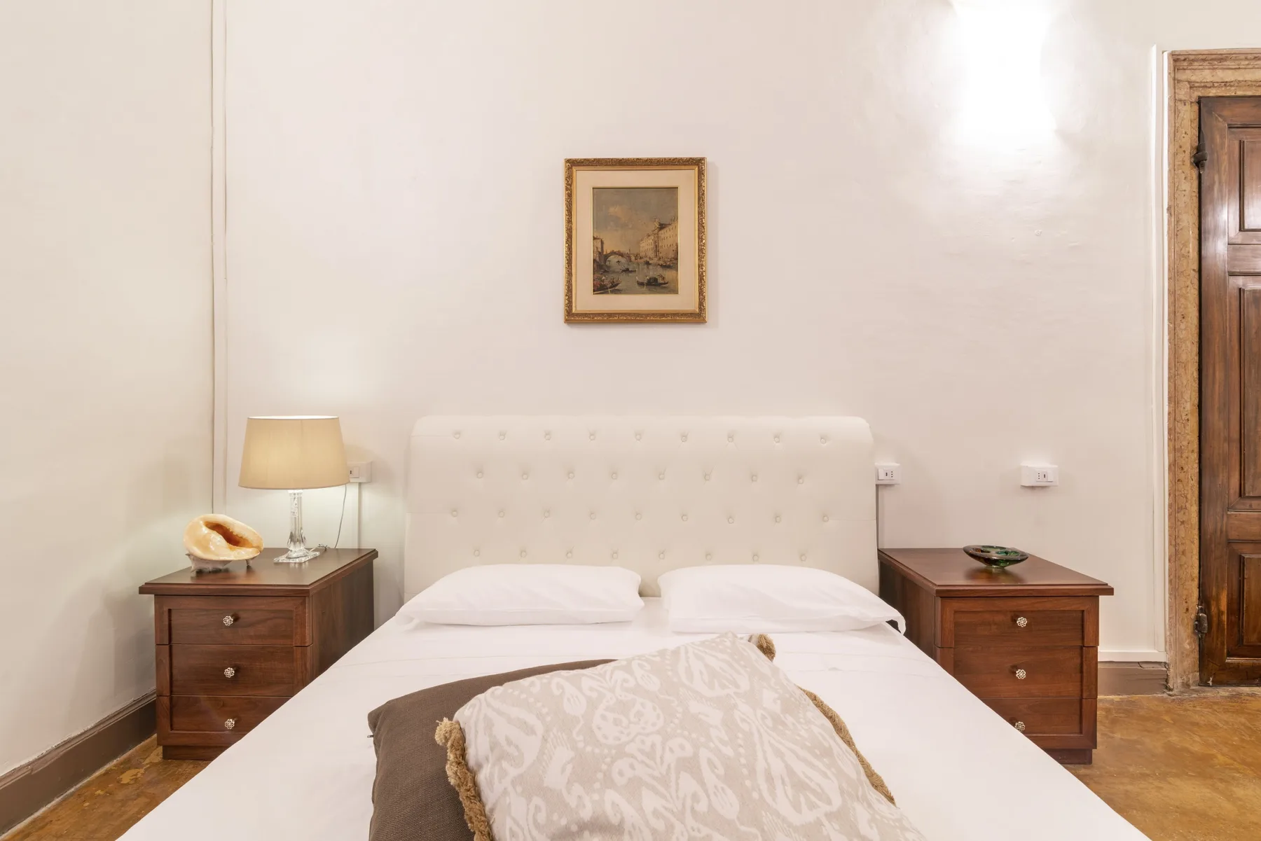 Un dormitorio con una cama, mesitas de noche y un cuadro sobre el cabecero.