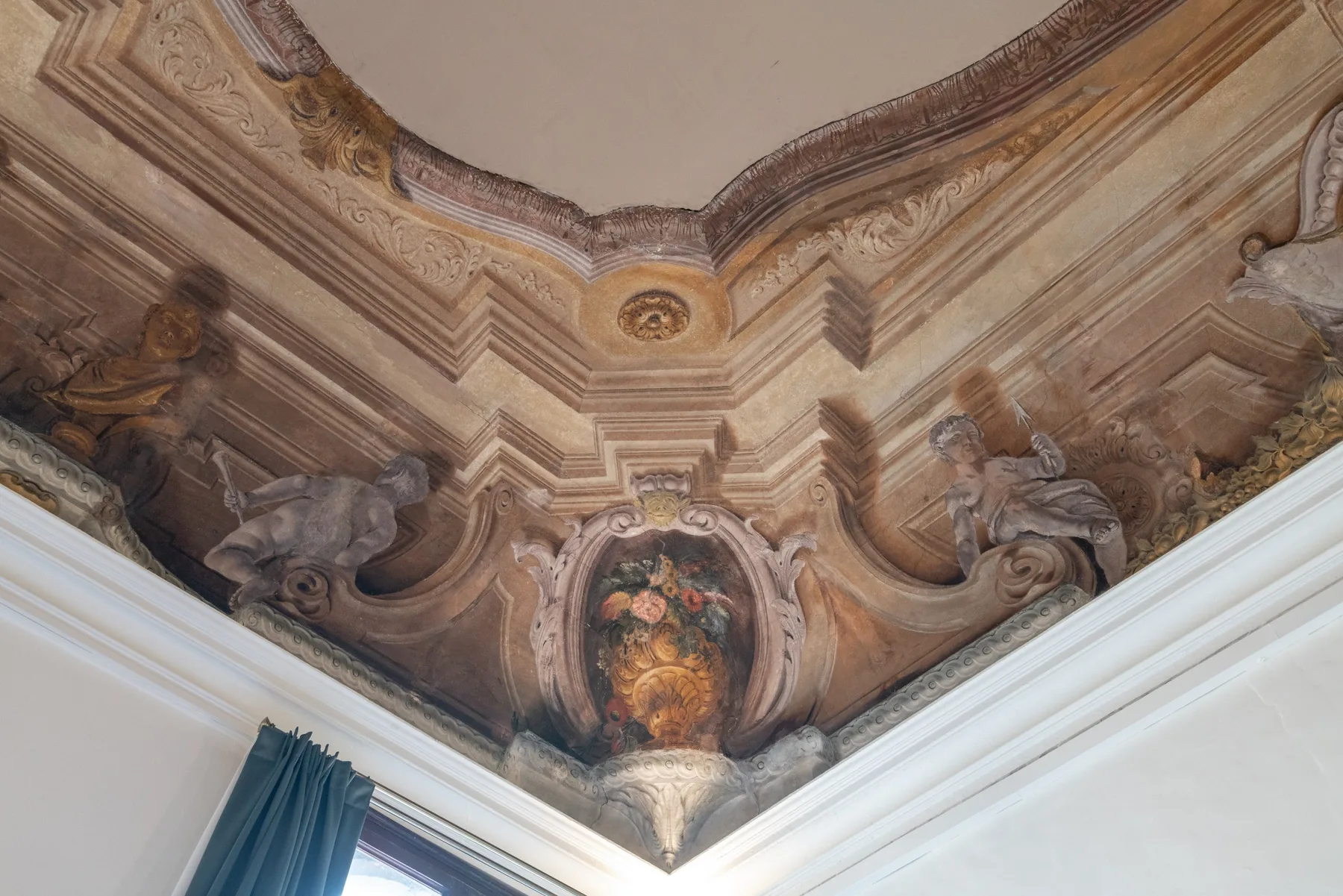 Un techo pintado ornamentado con figuras esculpidas y molduras decorativas.