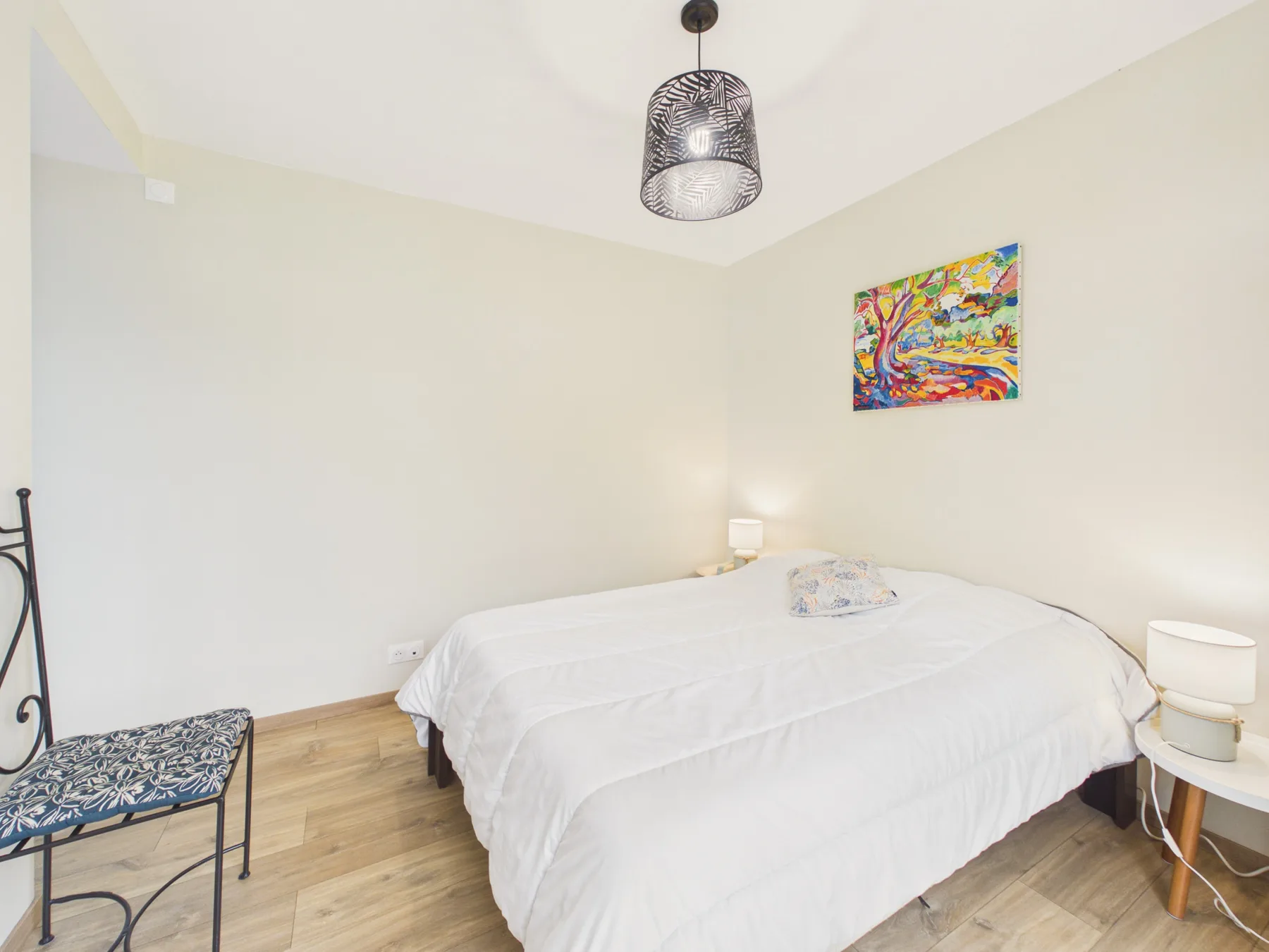 A bright bedroom with white bedding and colorful wall art.