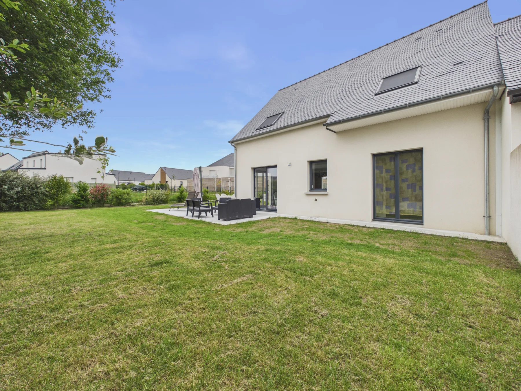 A house beside a broad lawn, with outdoor seating near the patio.