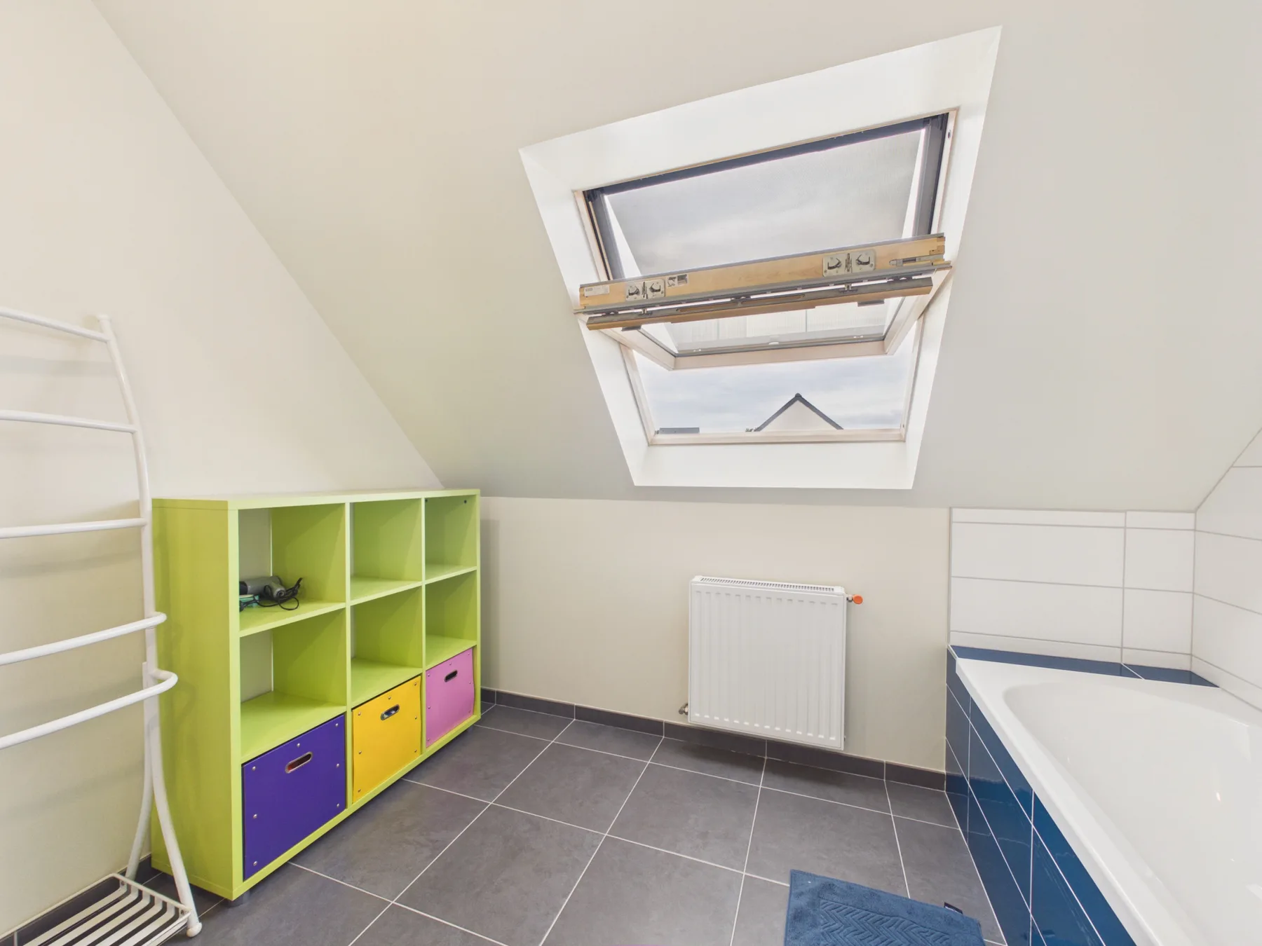 A tiled bathroom with a bathtub beneath a sloped ceiling and skylight.