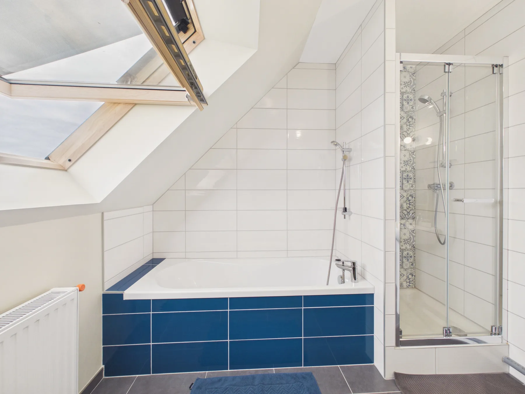 A bathroom with a bathtub beneath a sloped ceiling and a glass shower.