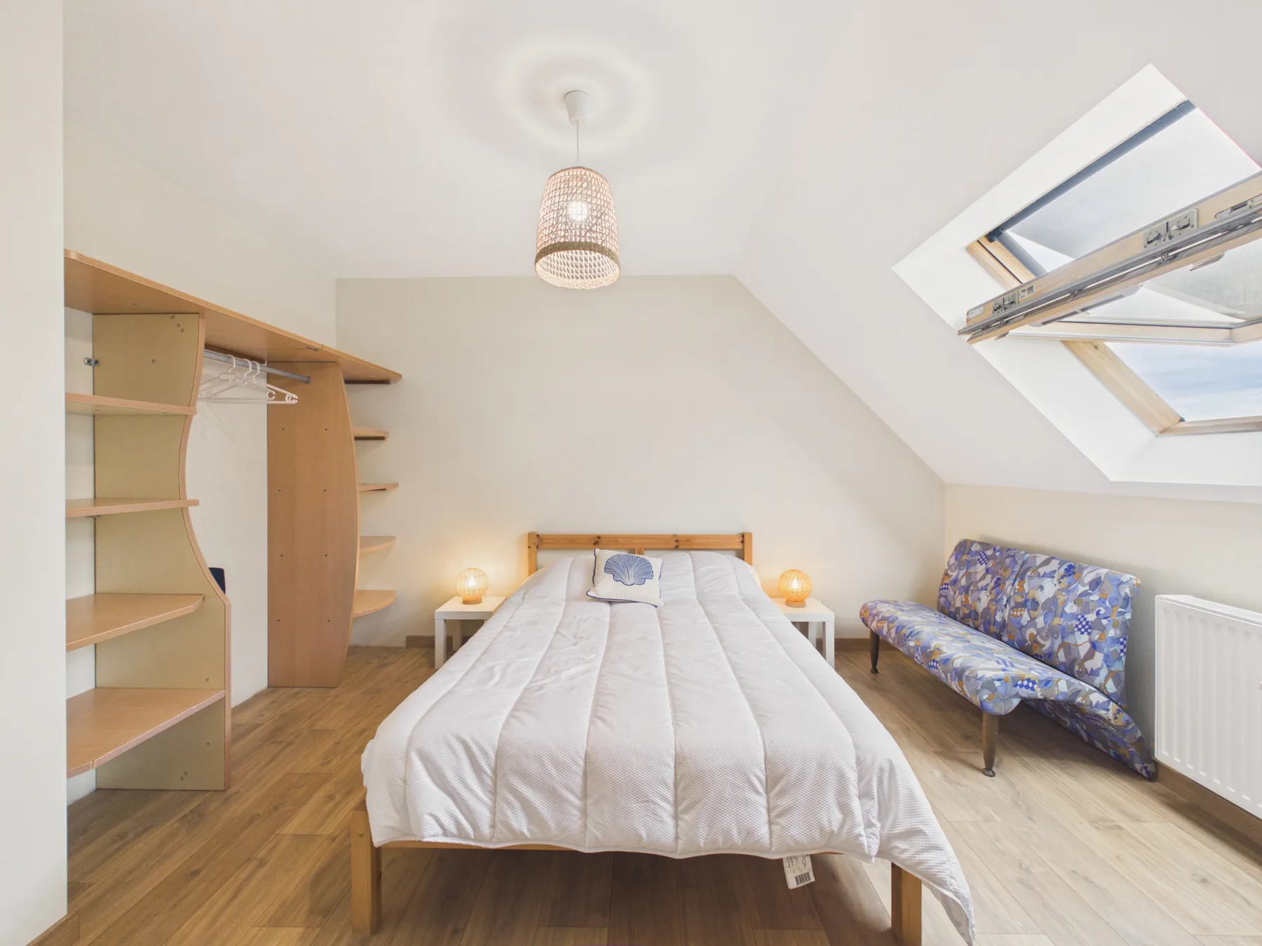 A bright bedroom with a bed, open shelving, and a skylight.