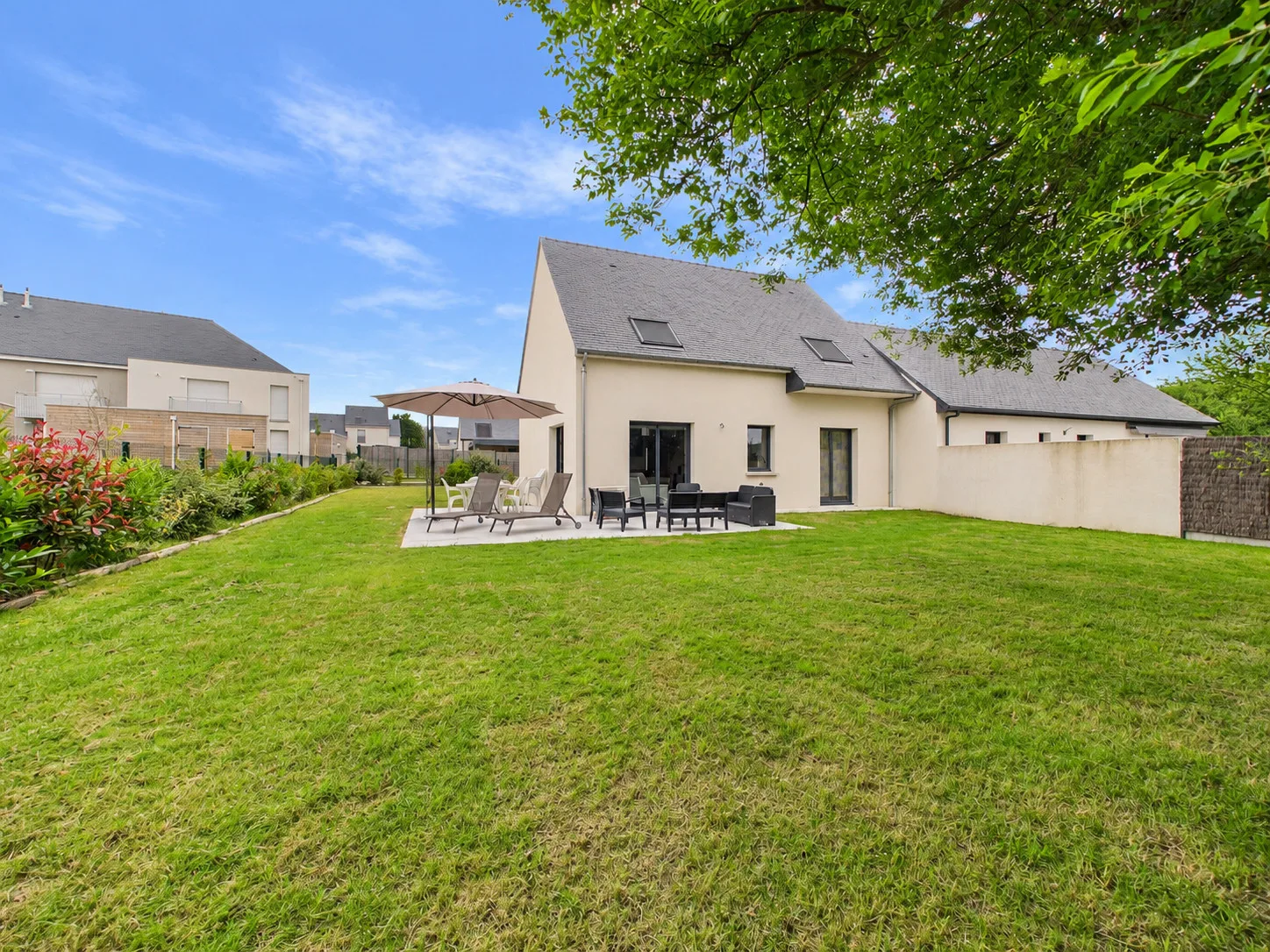 A house opens onto a broad green lawn and a patio seating area.