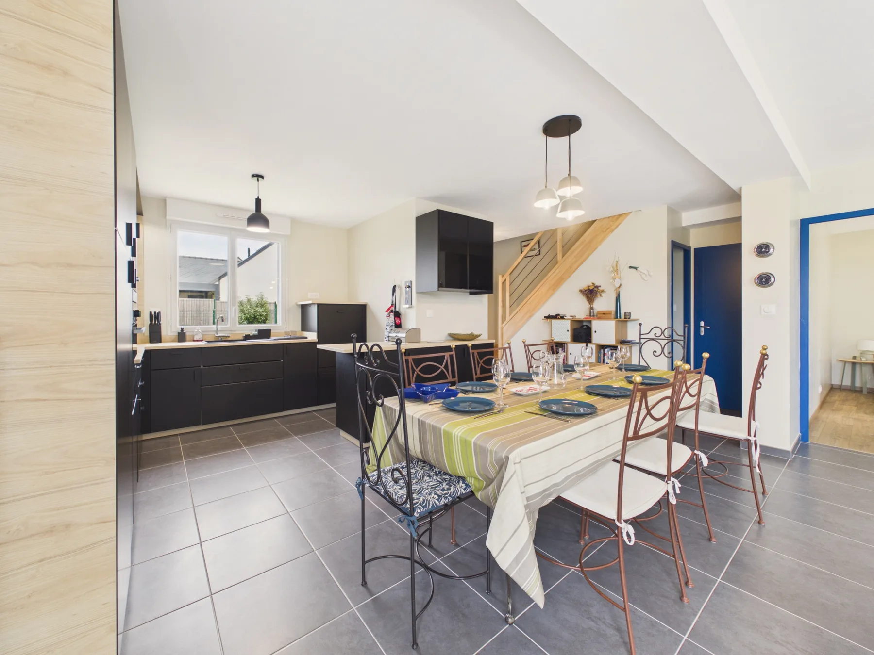 An open-plan dining and kitchen area with a long table and dark cabinets.
