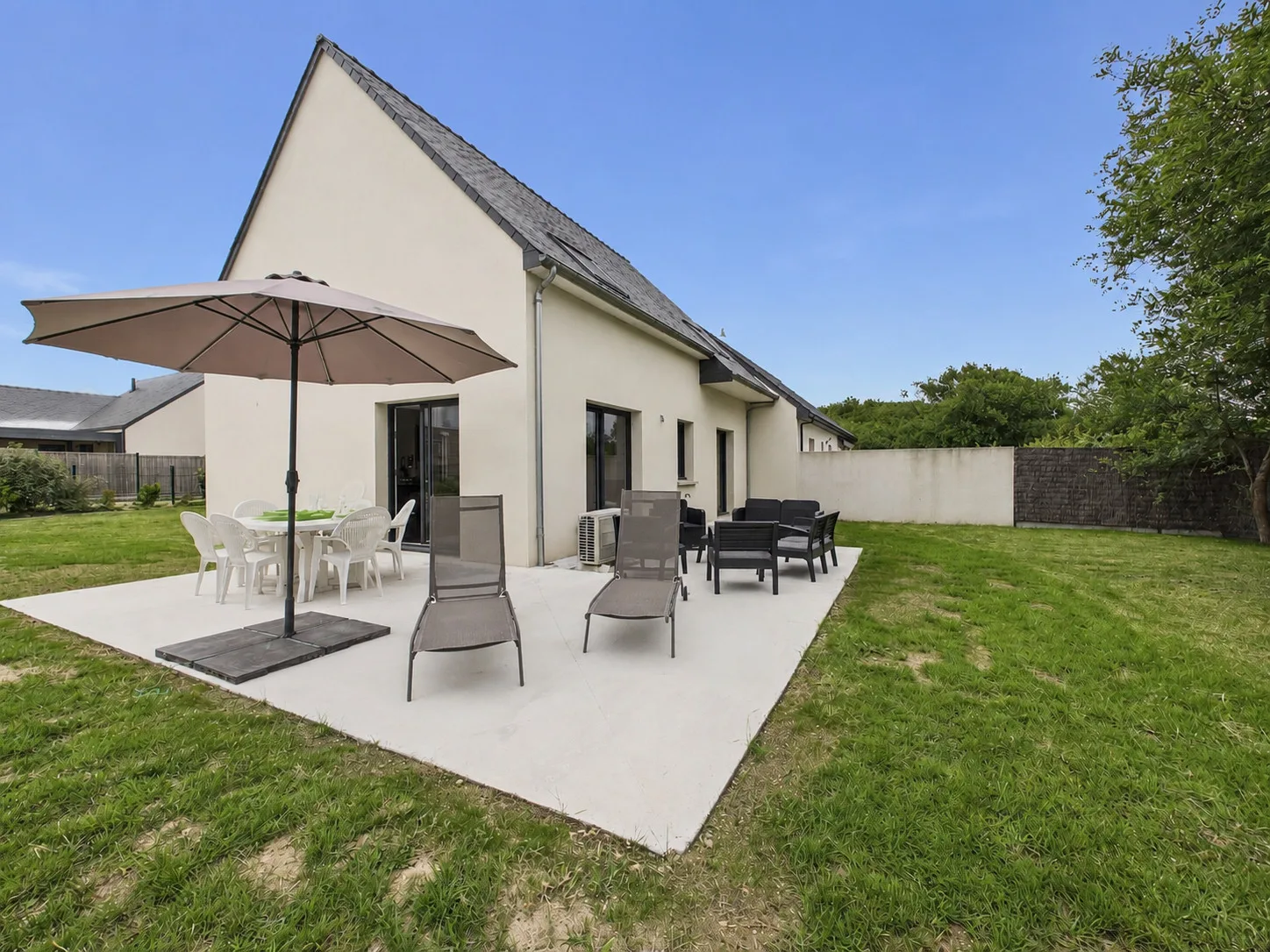Modern house with a patio, outdoor seating, and lawn.