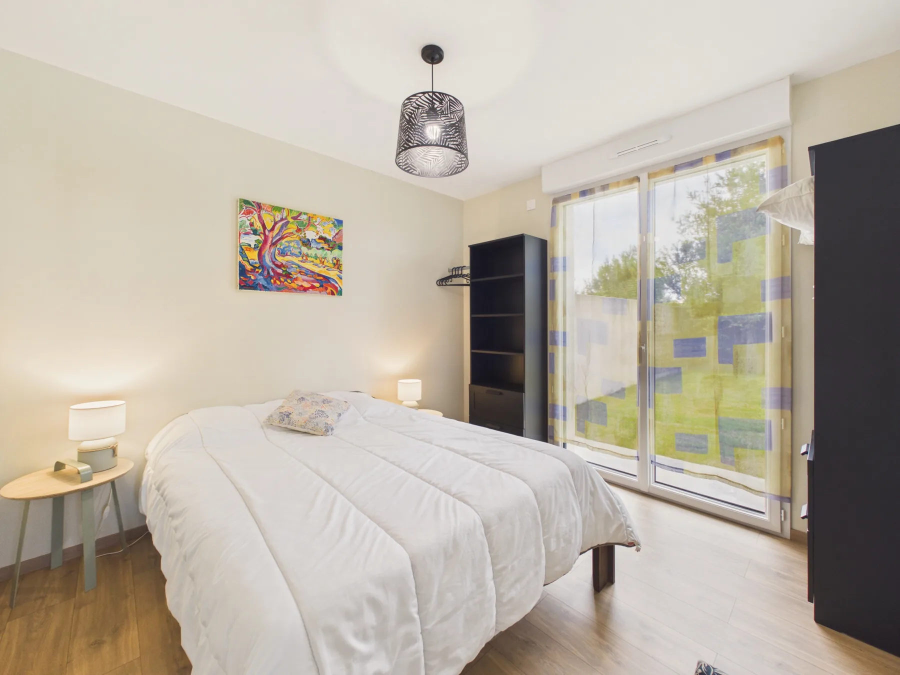A bedroom with a bed beside large windows overlooking greenery.