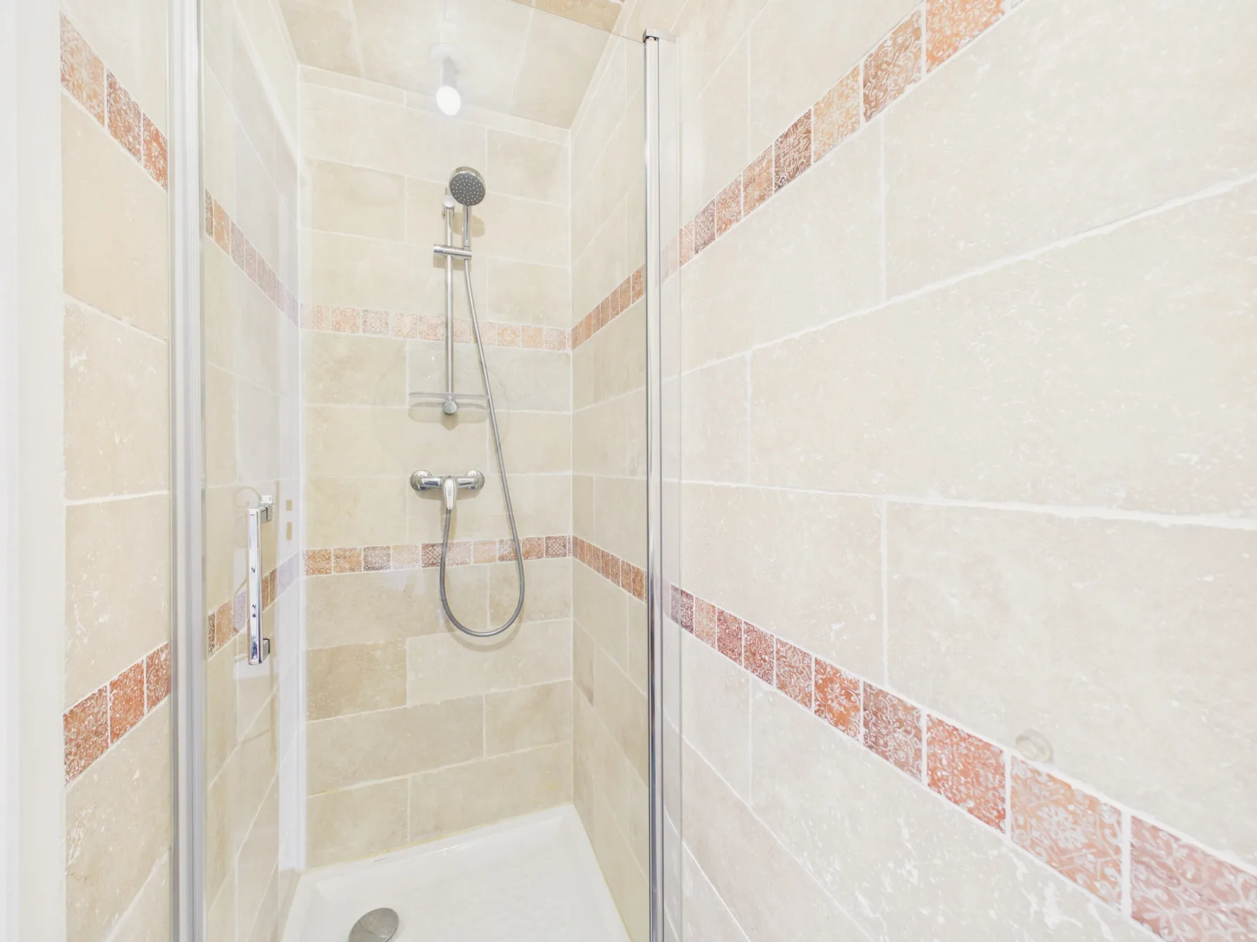 A tiled shower with a handheld showerhead and decorative horizontal bands.