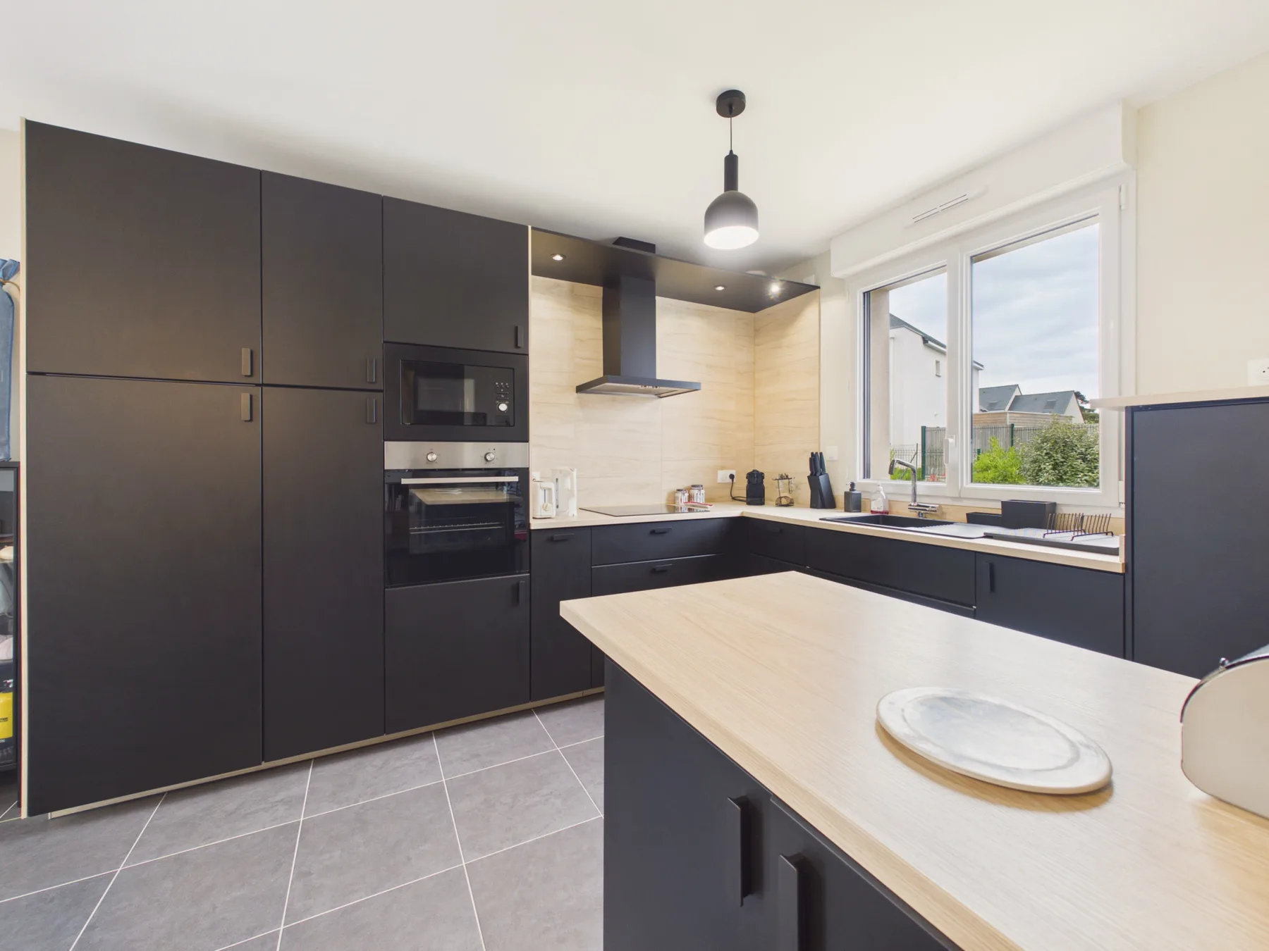 Modern kitchen with dark cabinets, a light countertop, and large windows.