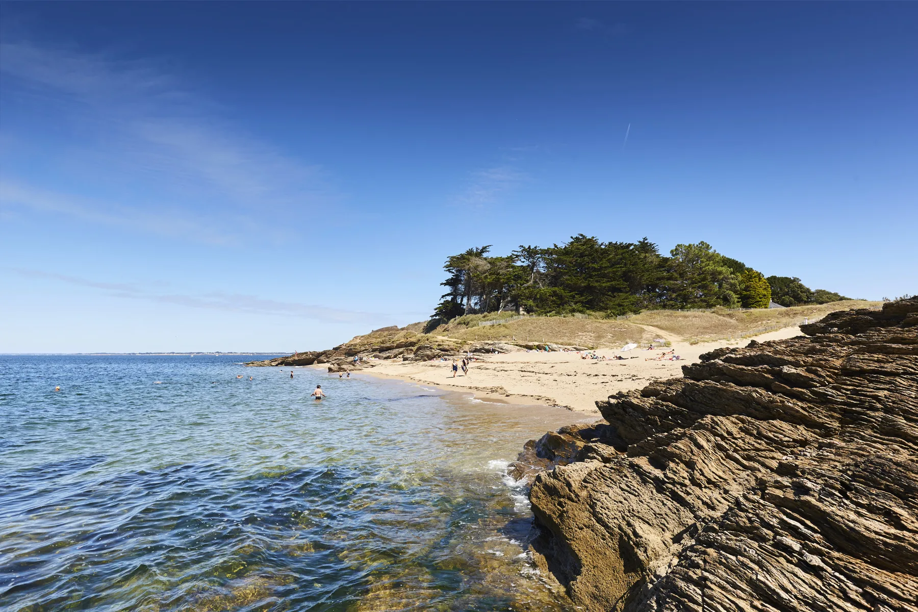 A sandy beach curves beside clear water and rocky outcrops.