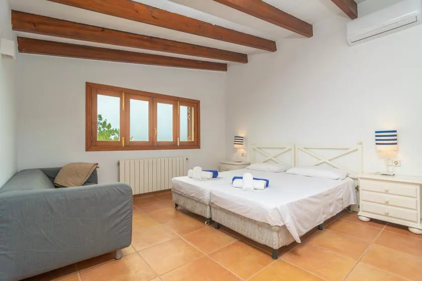 A bedroom with two beds, a window, and exposed wooden ceiling beams.