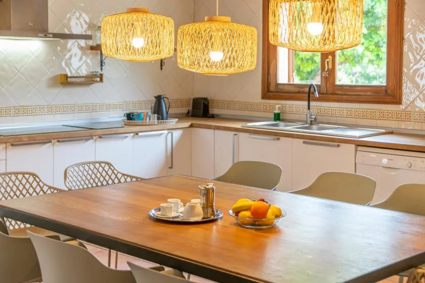A bright kitchen with a wooden dining table and woven pendant lights.