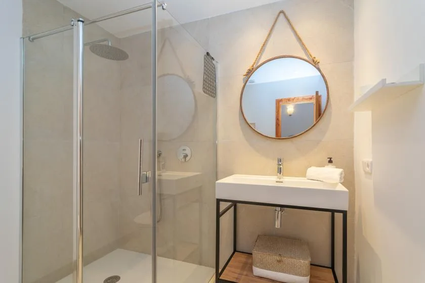 A bright bathroom with a glass shower and a vanity beneath a round mirror.