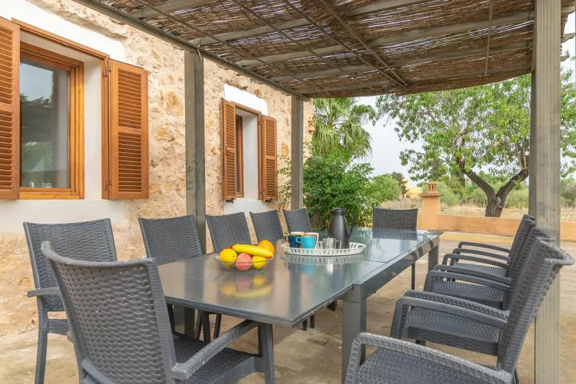 Una zona de comedor exterior a la sombra, con una mesa larga y asientos junto a un muro de piedra.
