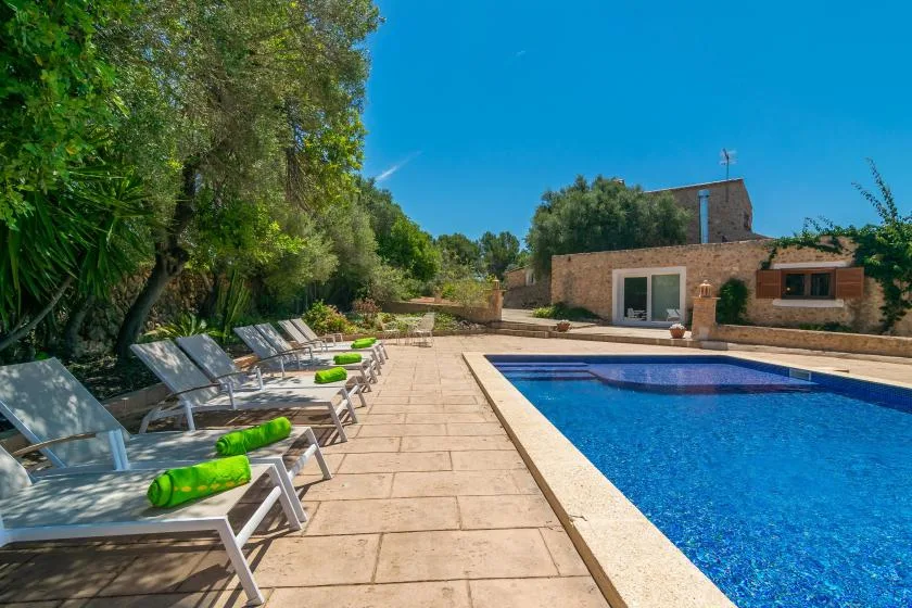 Una piscina al aire libre junto a un patio pavimentado con asientos reclinables.