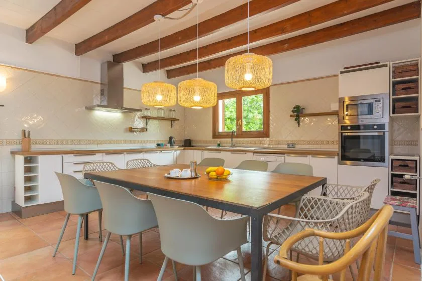 A spacious kitchen and dining area with a long table beneath wooden ceiling beams.