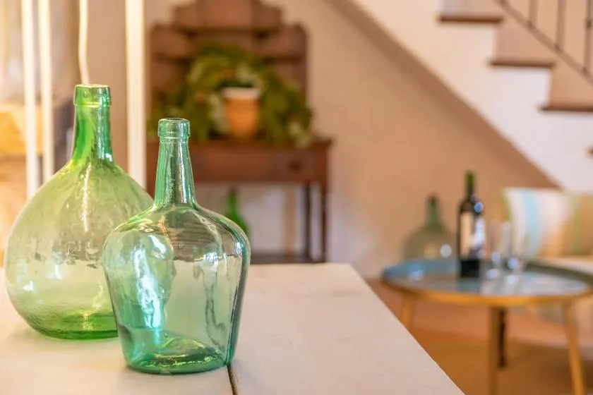 A bright interior dining area with glass bottles on a table and a staircase.