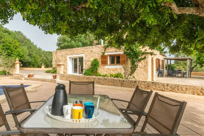 A stone house opens onto a shaded patio with outdoor seating and a set table.