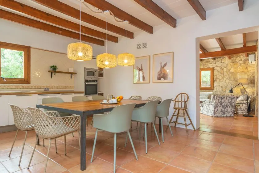 A dining area with a long table and woven pendant lights beside the kitchen.