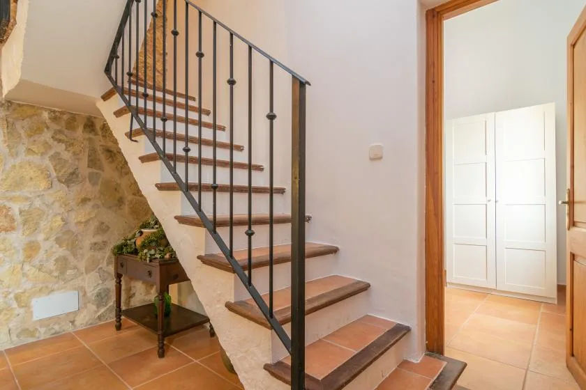 An indoor staircase with dark metal railings rises beside a stone wall.