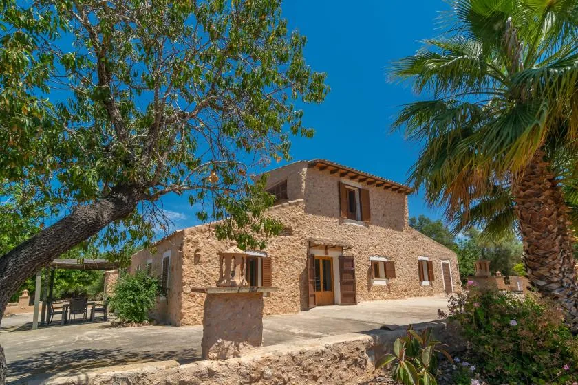 A stone house stands among leafy trees beneath a clear blue sky.
