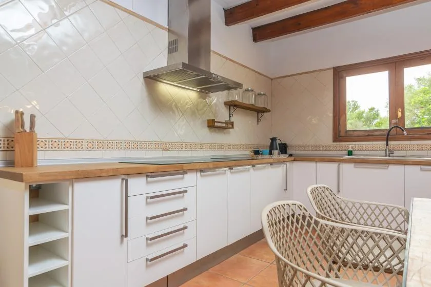 A bright kitchen with white cabinets, wooden countertops, and a window.