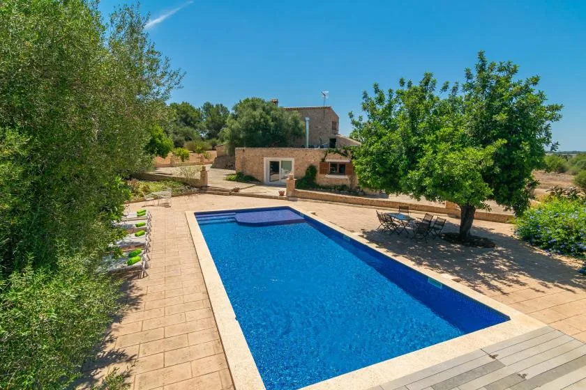 An outdoor swimming pool beside a paved patio and a stone house.