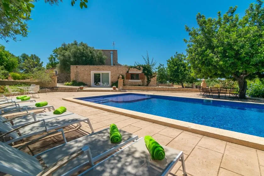 Una piscina al aire libre está rodeada por una terraza embaldosada y tumbonas.