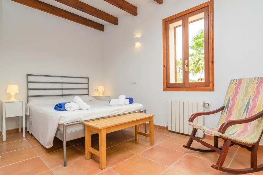 A bright bedroom with a bed, wooden table, and rocking chair.