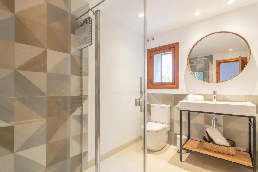 A bathroom with a glass shower, toilet, and sink beneath a round mirror.