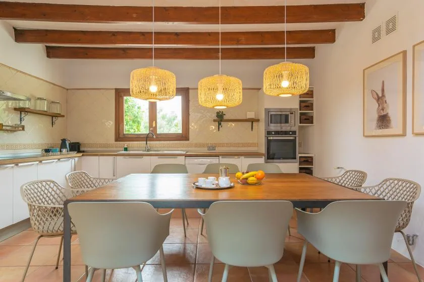 A dining area with a long table, pale seating, and pendant lights.