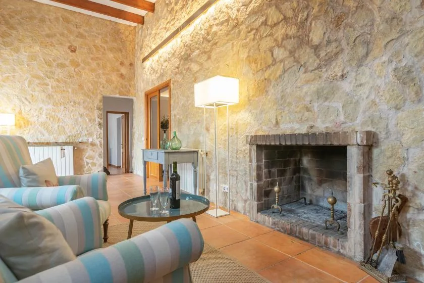 A rustic living room with striped seating and a large stone fireplace.