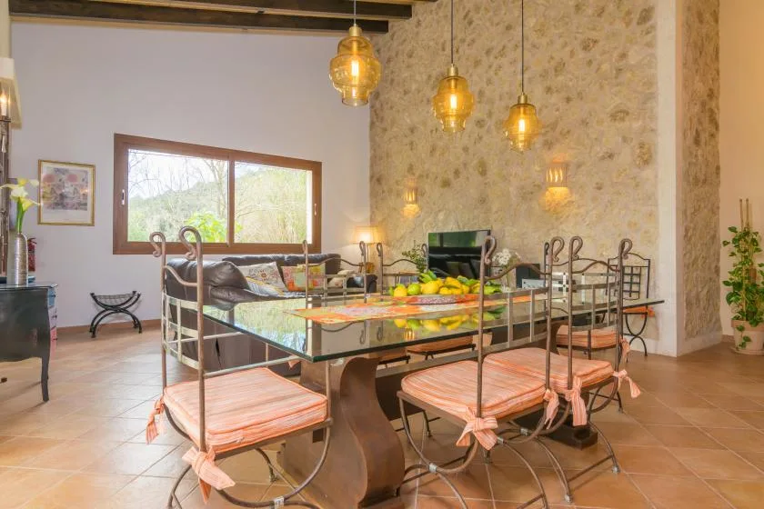 Un comedor con una larga mesa de vidrio y asientos metálicos bajo lámparas colgantes.
