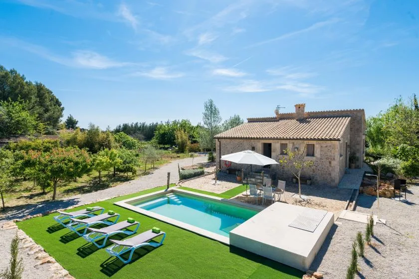 Una casa de piedra da a una piscina y una zona de descanso en un jardín ajardinado.
