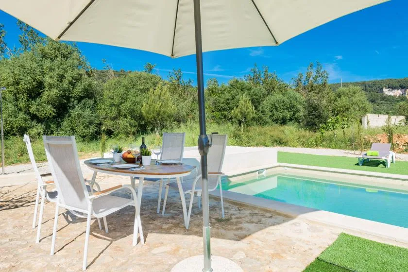 Una piscina al aire libre junto a una zona de comedor en el patio, con asientos bajo una sombrilla grande.