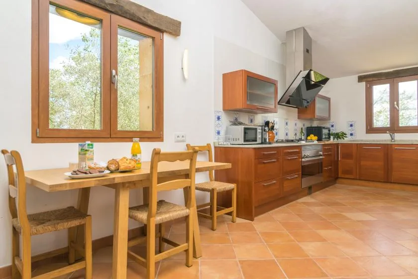 Una cocina y comedor con gabinetes de madera, una mesa y ventanas grandes.
