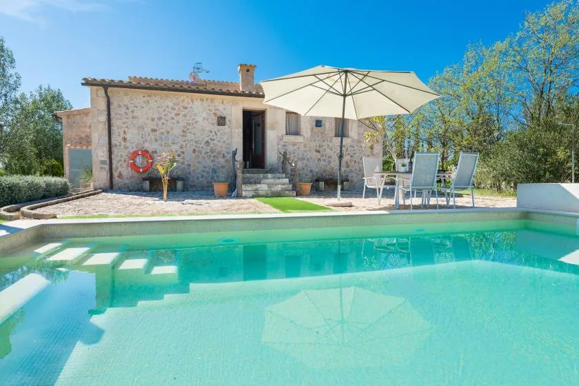 Una piscina junto a una casa de piedra, con una zona de estar exterior sombreada.