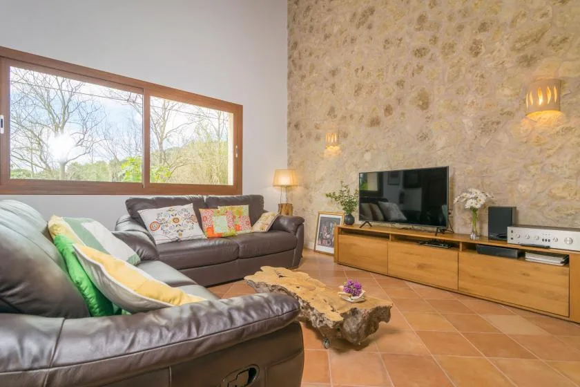 Una sala de estar con asientos oscuros, un televisor y una ventana amplia.