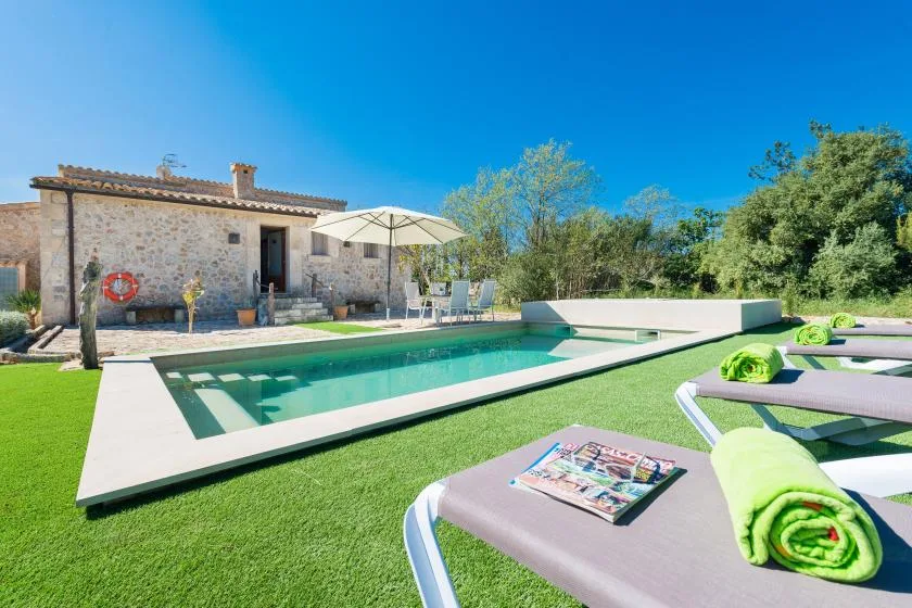 Una piscina junto a una casa de piedra, con tumbonas sobre el césped.