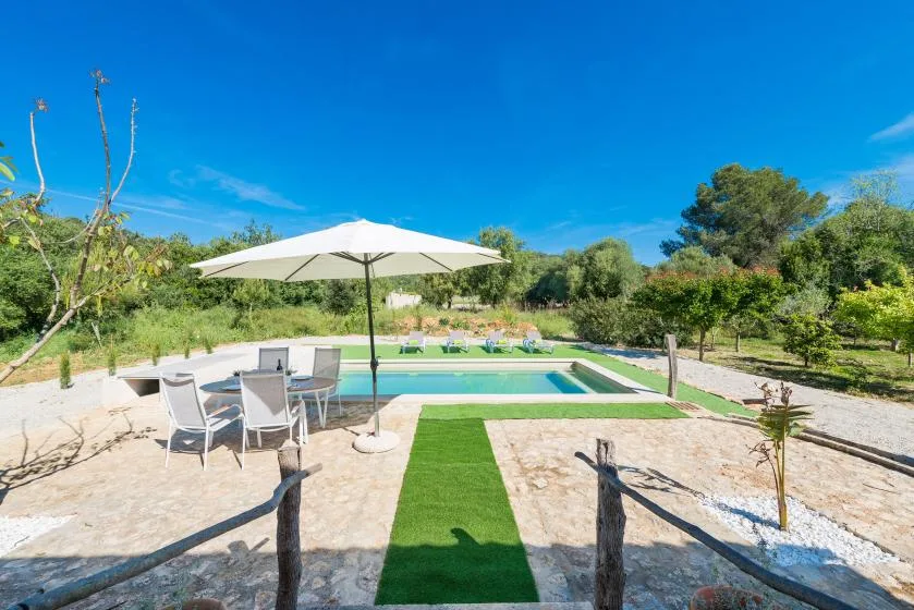 Una piscina al aire libre está junto a un césped verde y una zona de estar a la sombra.