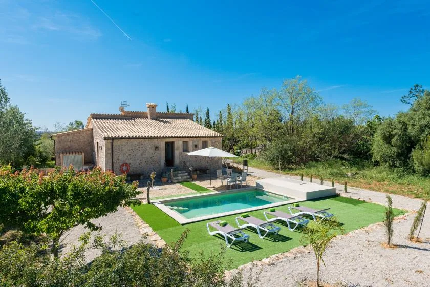 Una casa de piedra da a una piscina y un césped verde.