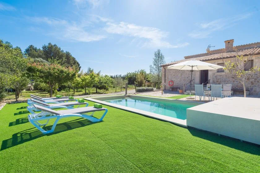 Una piscina al aire libre junto a un césped y tumbonas.