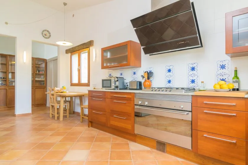 Una cocina luminosa con gabinetes de madera, una mesa de comedor y una campana extractora grande.