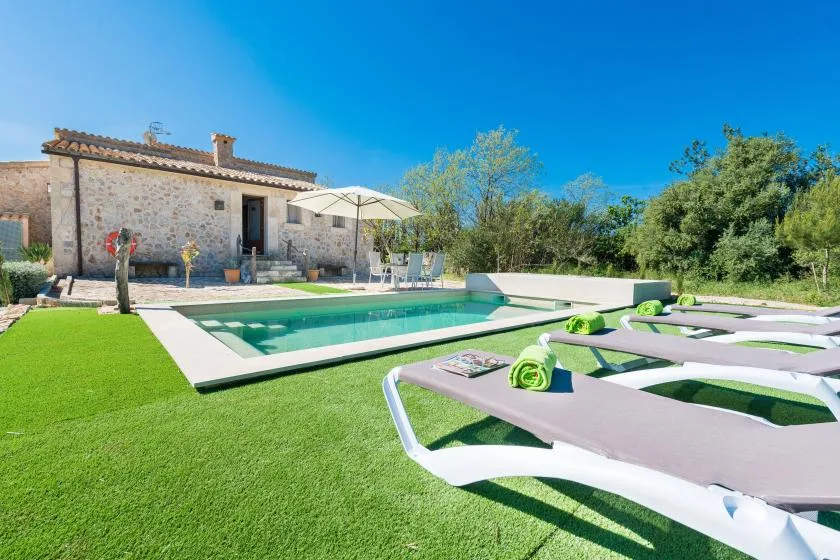 Una piscina al aire libre junto a una casa de piedra, con tumbonas sobre el césped.