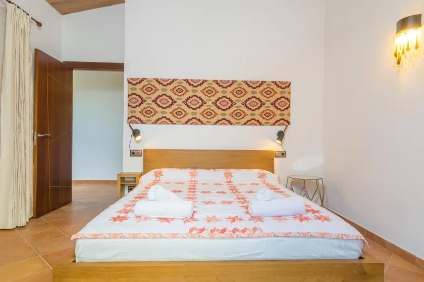 Un dormitorio con una cama vestida con ropa de cama blanca y estampada en naranja.